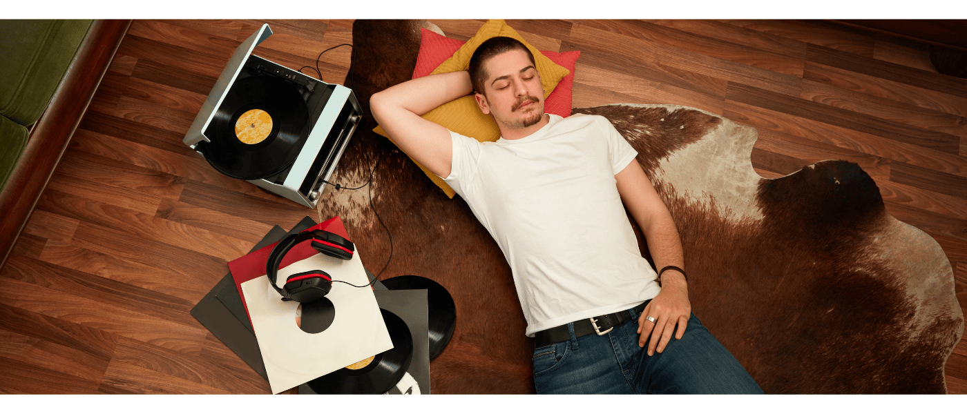 A man lying on floor next to a record player, enjoying the music