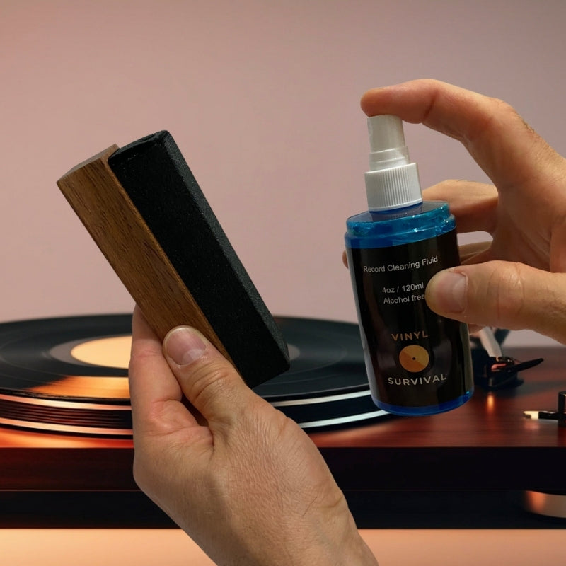 a hand holding a 120ml bottle of vinyl survival record cleaning fluid, about to spray a velvet album cleaning brush. With a record player in the background